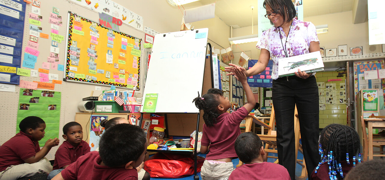 Young kids on rug in classroom with teacher reading